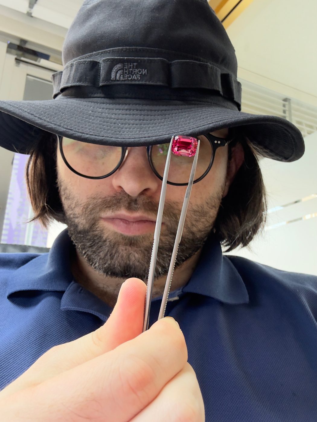 Holding a pink gemstone in tweezers up for inspection