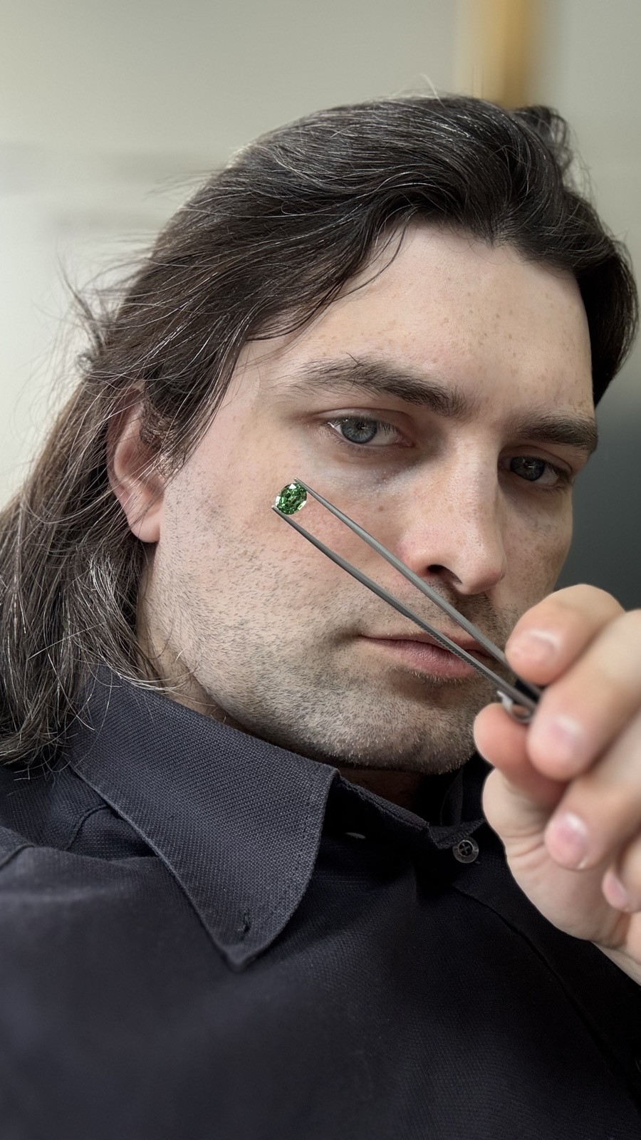 A green stone in the tweezers, held to the eye